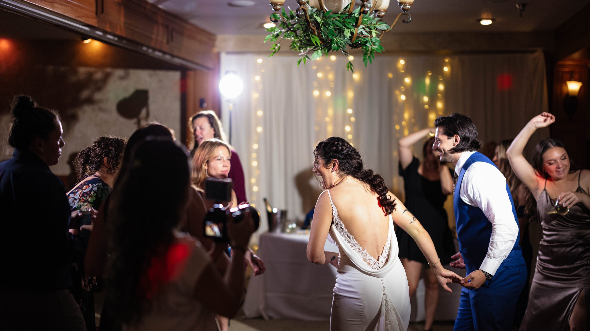Guests with arms raised on a packed reception dance floor under string lights