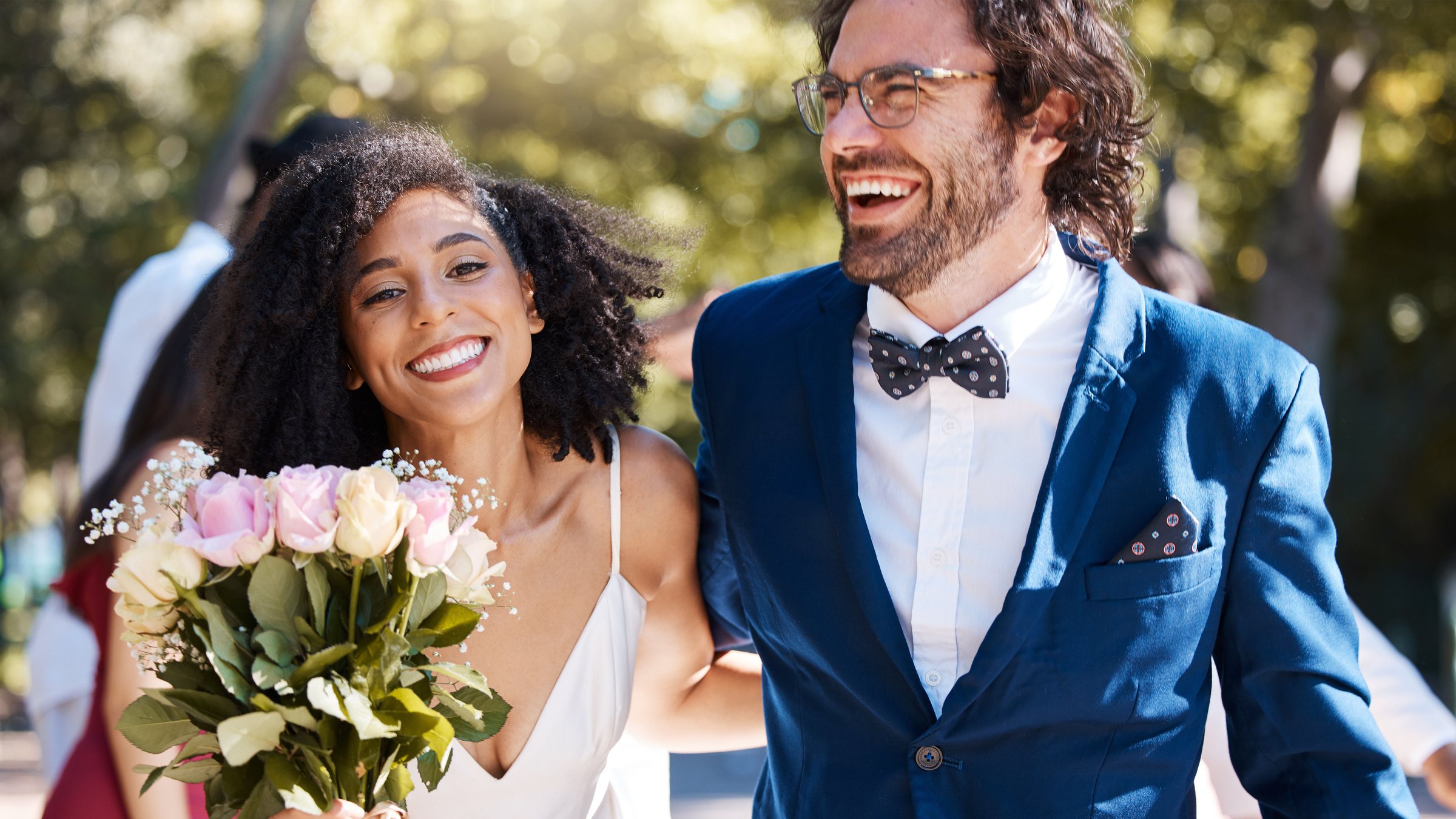 Bride and groom laughing together outdoors, bride holding a pink rose bouquet