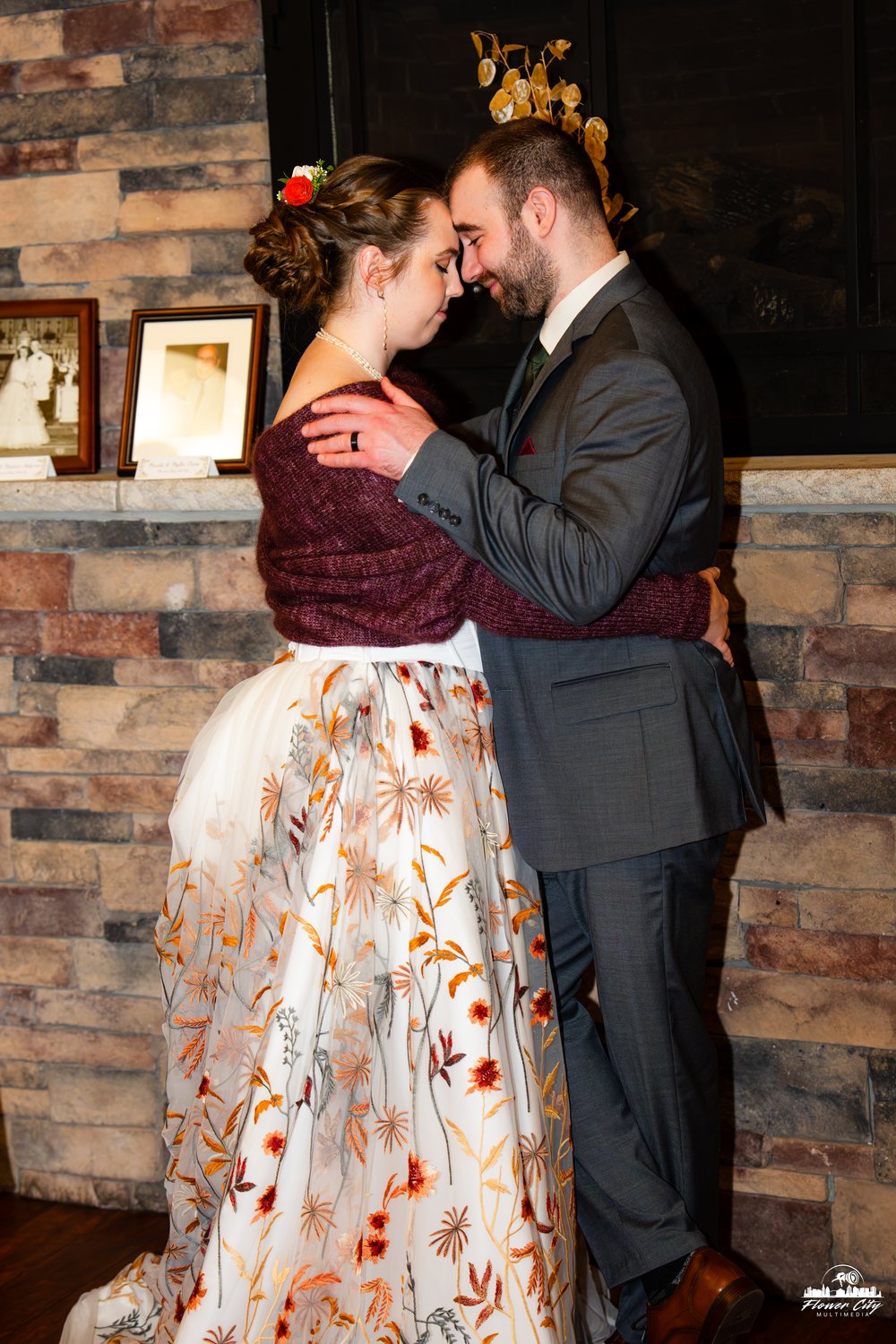 Newlyweds kissing by a brick fireplace, bride in a floral gown