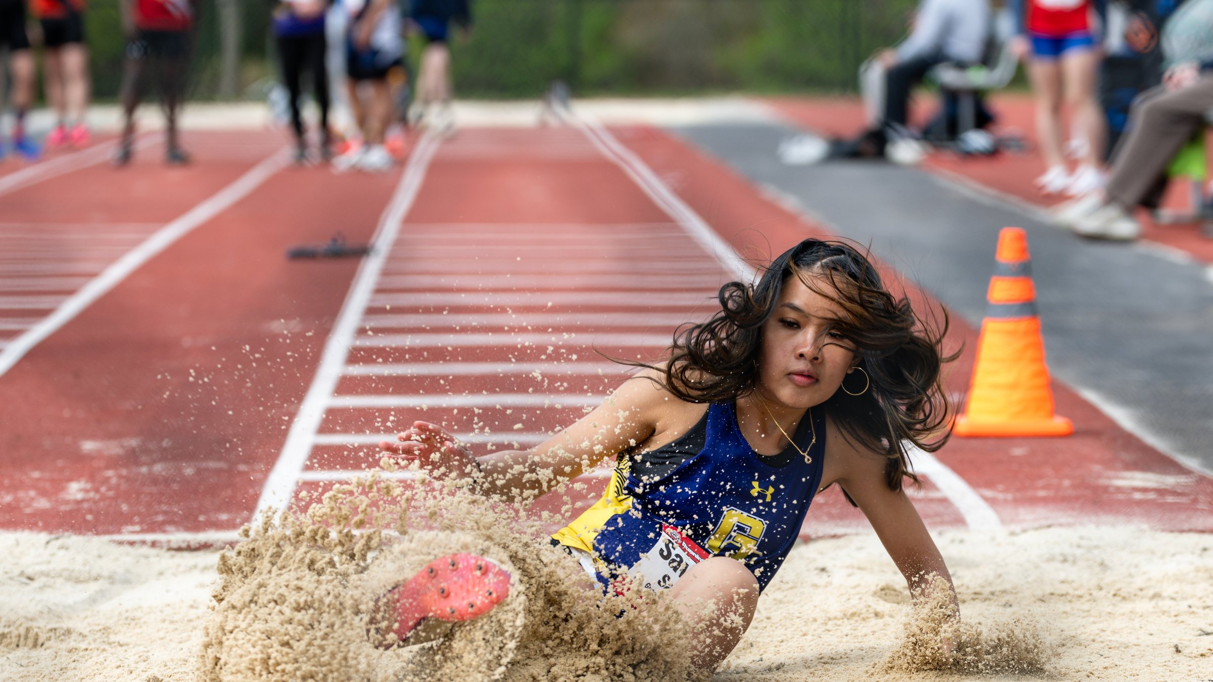 Long jumper with flying hair landing in a spray of sand at the Hilton track and field invitational