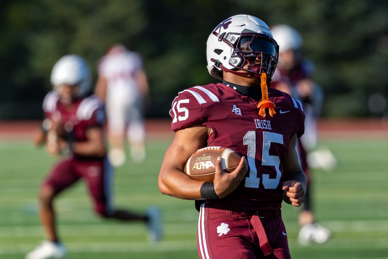 Football ball carrier wearing number 15 in a maroon jersey running upfield