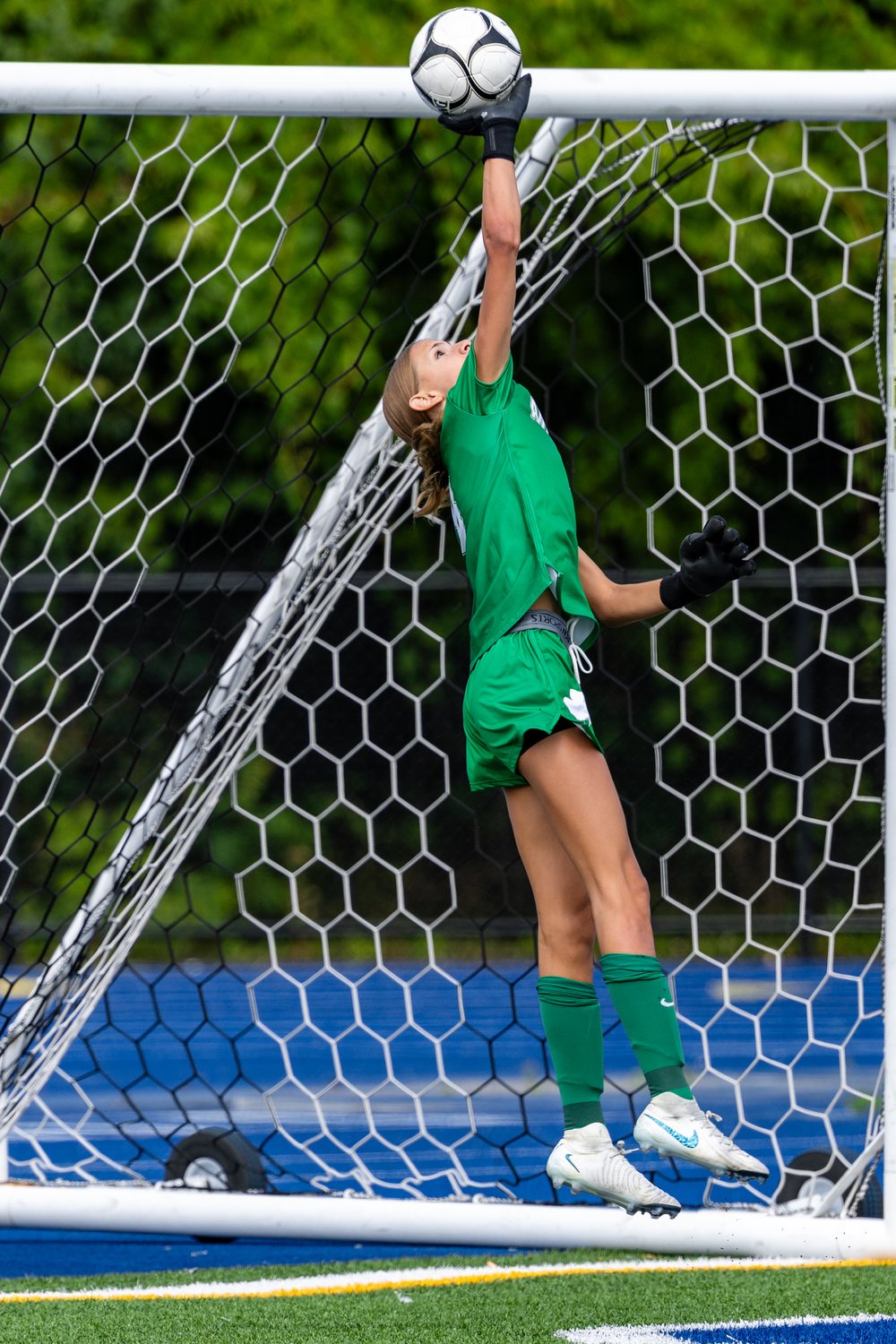 Soccer goalkeeper in green leaping to tip a high shot away from the net
