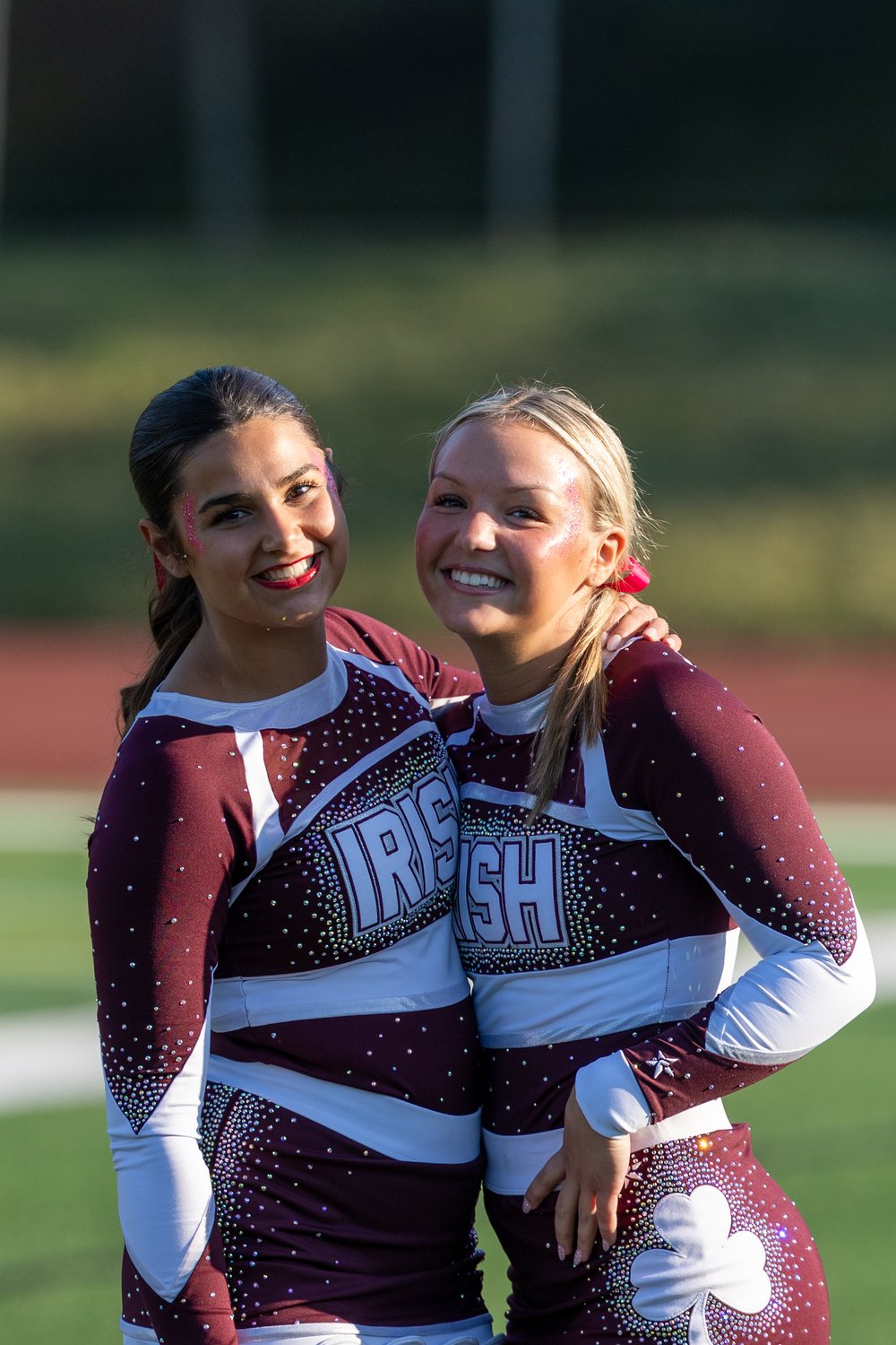 Two cheerleaders smiling cheek to cheek at a varsity football game