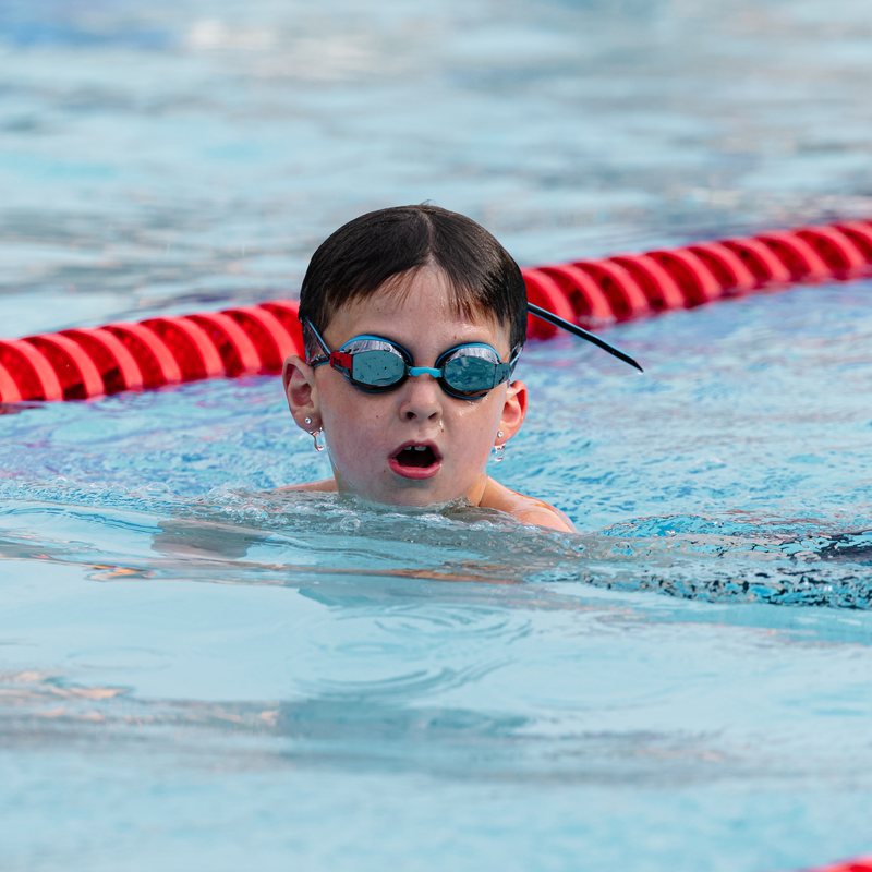 Young swimmer in goggles peeking up from the water beside the lane line