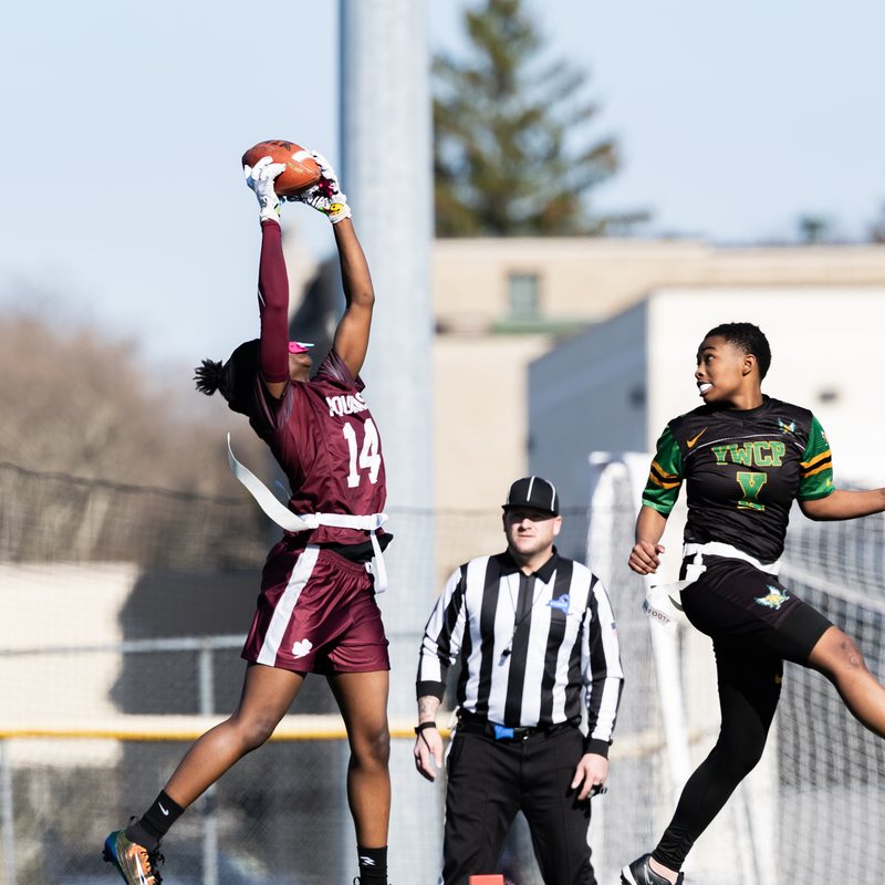 Flag football player leaping high to catch the ball as a defender closes in
